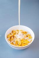 A close-up of fresh milk being poured into a bowl of golden cornflakes photo