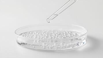 Clear liquid droplet falling into petri dish with bubbles in scientific experiment photo