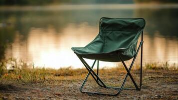 Green portable camping chair on lakeside at sunset with tranquil reflections in water photo