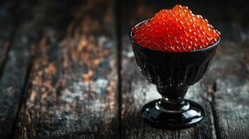 Luxurious red caviar in elegant black glass bowl on rustic wooden table photo