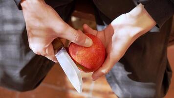 Close-up of hands peeling a red apple with a sharp knife, precision knife work in a rustic kitchen setting with warm lighting and natural textures video