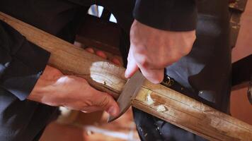 Close-up of hands carving a wooden plank with a sharp chisel, detailed woodworking craftsmanship in a rustic workshop setting with warm lighting and wood shavings scattered around video