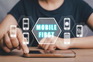 Mobile first concept, Person hand using smart phone with mobile first icon on virtual screen, Digital marketing, office desk. photo