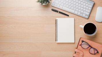 Wooden desk workplace with keyboard computer, mouse, notebook, pen, eyeglass, notebook and cup of coffee, Top view flat lay with copy space. photo