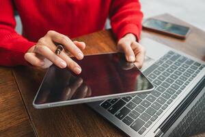 Hands interacting with a tablet next to a laptop on a wooden desk, showcasing modern technology in a casual setting. photo