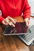 Close-up of hands holding a tablet and using a laptop, showcasing modern technology in a casual environment. photo