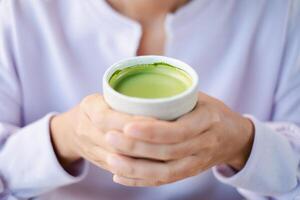 A person holding a cup of vibrant matcha green tea, showcasing warmth and relaxation in a serene environment. photo