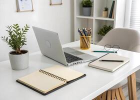 A white desk with a laptop, notepad, and a plant photo