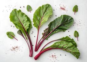 Several Swiss chard leaves with vibrant green color and deep red stems are spread on a white surface photo