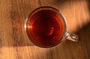 Warm brew in a glass mug resting on a wooden table illuminated by soft afternoon light photo
