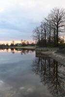 Calm reflections at dusk by the serene lakeside with trees and soft sunset hues photo