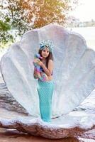 A smiling little girl in a mermaid costume in a large seashell, photo