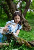 Young caucasian girl in blue dress with plush rabbit in green forest setting photo