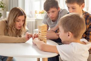A cute mother and three sons are enthusiastically playing a board game made of wooden rectangular blocks photo
