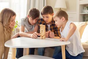 A smiling woman and three boys are enthusiastically playing a board game made of wooden rectangular blocks photo