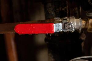 Red lever handle on metal pipe with water droplets in industrial setting photo