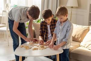 Three boys, in home enthusiastically play a board game made of wooden rectangular blocks photo