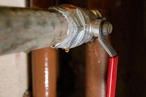 Leaking pipe valve with metal fittings and red handle in need of repair photo