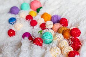 A lot of colorful knitting yarn and a luminous garland in the form of balls lie on fluffy blanket. photo