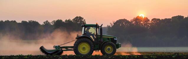 Sunset tractor plowing in misty field with vibrant horizon photo