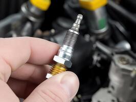 Close-up of a hand holding a spark plug, with engine components visible in the background, highlighting automotive maintenance and repair. photo