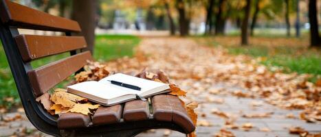 A tranquil park scene featuring a bench adorned with autumn leaves and an open notebook, inviting creativity amidst nature. photo