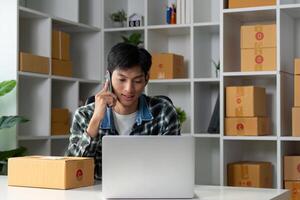 Young entrepreneur conducting business call while managing online sales, using laptop in modern workspace with product boxes. photo