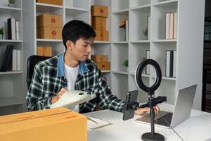 Young entrepreneur managing online sales while showcasing product, using laptop and smartphone in modern workspace. photo