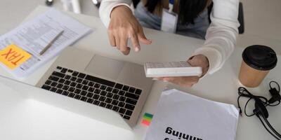 Close-up of a young professional calculating tax deductions using a calculator and laptop. photo