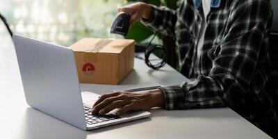 Close-up of a young man using a laptop while scanning a package for shipping. photo