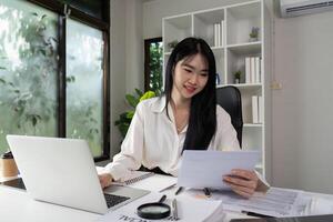 Tax Document Review. A smiling professional reviewing tax documents while seated at a desk with a laptop and paperwork. photo