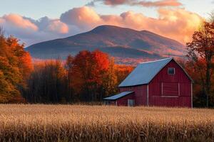 Red barn standing in a cornfield with colorful autumn foliage and mountain in the background during sunset photo