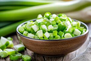 Bowl of chopped scallions resting on wooden table with whole scallions in background photo