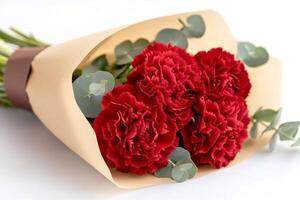 Bouquet of red carnations wrapped in brown paper lying on white background photo