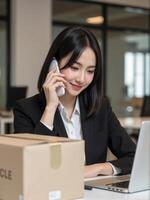 A woman in a business suit talking on the phone while sitting at a desk with a laptop photo