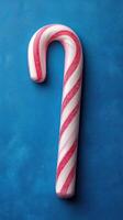 Brightly colored candy cane resting on a textured blue background brings festive vibes during the holiday season photo