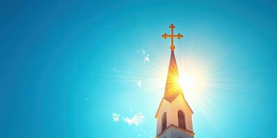 Bright sunlight reflects off the cross atop a church steeple against a clear blue sky during a sunny day photo