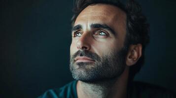 Pensive man gazes upward with thoughtful eyes He has a dark beard and hair against a dark background and hopeful expression photo