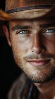 Close-up of a young man with striking blue eyes wearing a cowboy hat, showcasing confidence and charm in a rustic setting photo