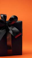 Elegant black gift box with a ribbon on a vibrant orange background for a festive occasion photo