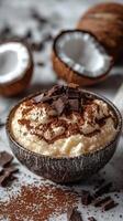 Creamy dessert with chocolate shavings and coconut in a rustic bowl placed on a textured surface photo