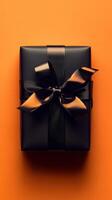 Elegant black gift box with a glossy ribbon on a vibrant orange background ready for a special occasion photo