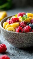 Freshly prepared fruit salad with raspberries, blueberries, and pineapple in a textured bowl on a stone surface photo