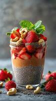 Delicious chia seed pudding topped with fresh strawberries and cashews in a clear glass cup photo