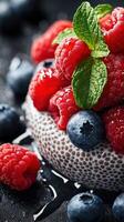 Fresh raspberries and blueberries arranged beautifully in a bowl with mint leaves on a dark background photo