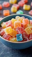Colorful gummy candies in a blue bowl on a dark surface surrounded by scattered treats photo