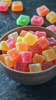 Colorful candy squares in a wooden bowl on a dark surface with scattered sweets in the background photo