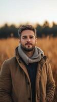 Handsome man standing in a golden field during sunset, wearing a warm coat and scarf, expressing confidence and calmness photo