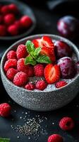 Fresh berries and fruits served in a textured bowl with mint garnish on a dark background photo