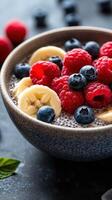 Fresh fruit and chia seed bowl with bananas, raspberries, and blueberries on dark background photo
